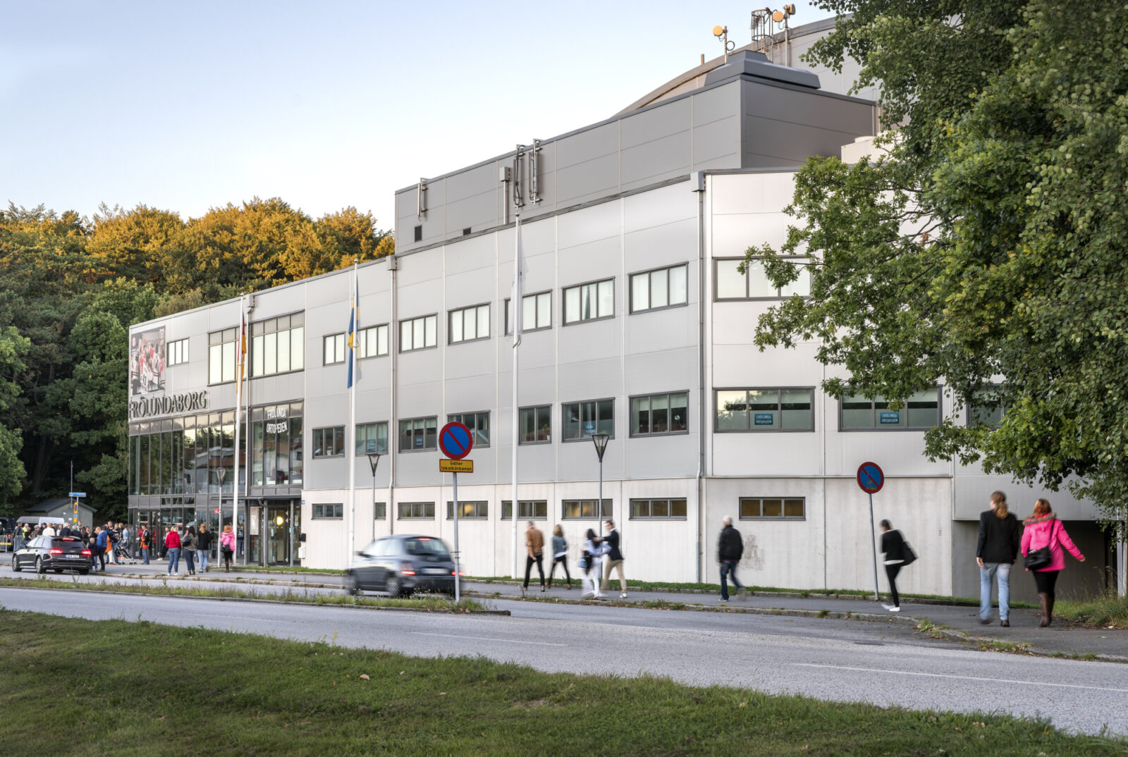 Människor promenerar förbi en grå hockeyarena.