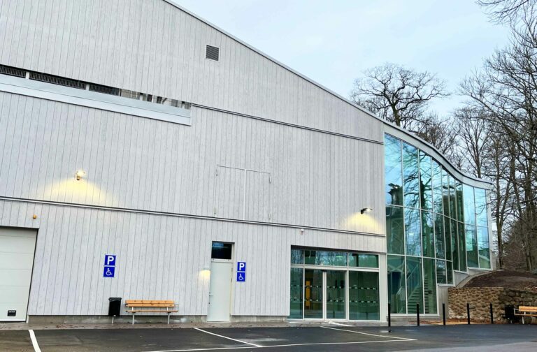 Utsidan av en grå träbyggnad med ett stort glasparti.